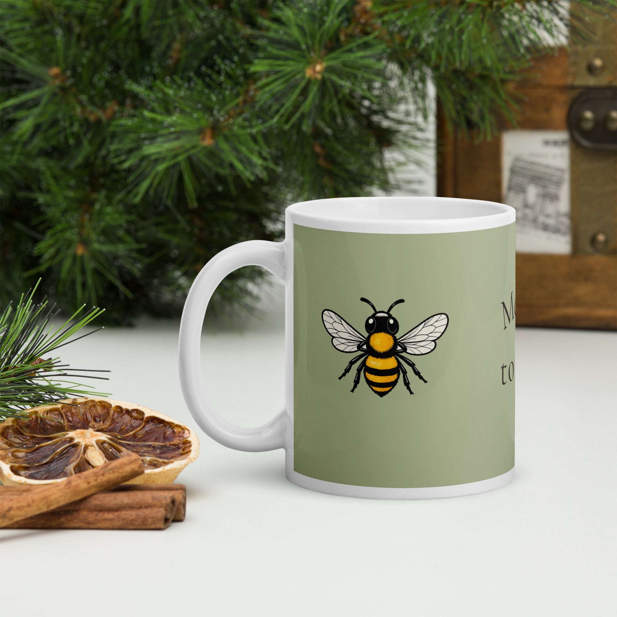 Sage green ceramic mug with bee illustration and white handle on a surface