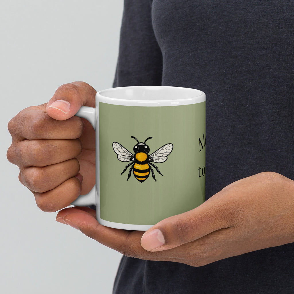 Sage green ceramic coffee mug held in two hands, bee illustration on front