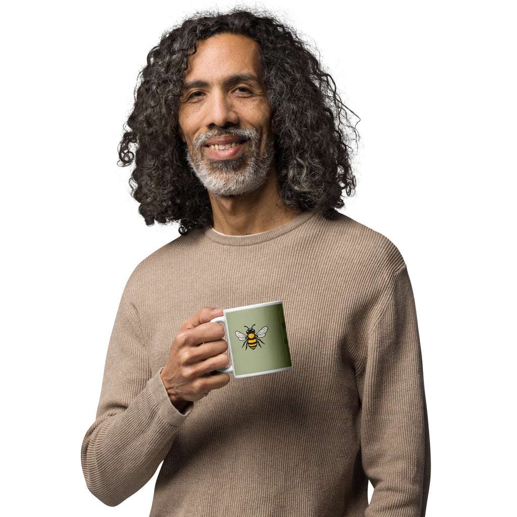 Sage green ceramic coffee mug with bee illustration, held at chest height