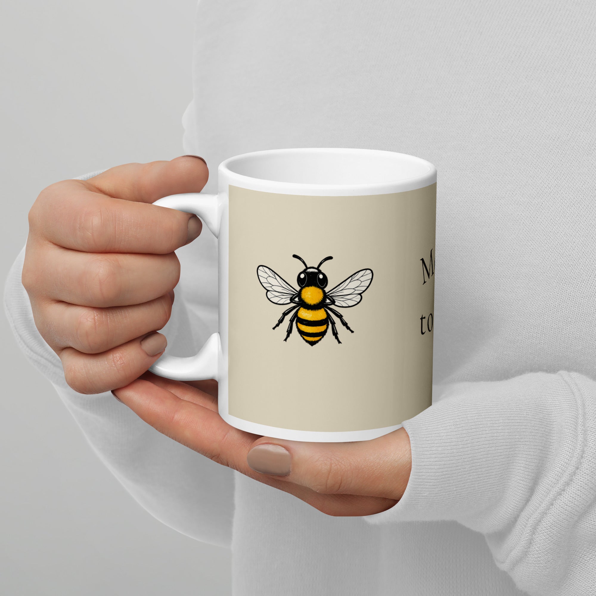 Light beige ceramic coffee mug with white handle and bee illustration on front