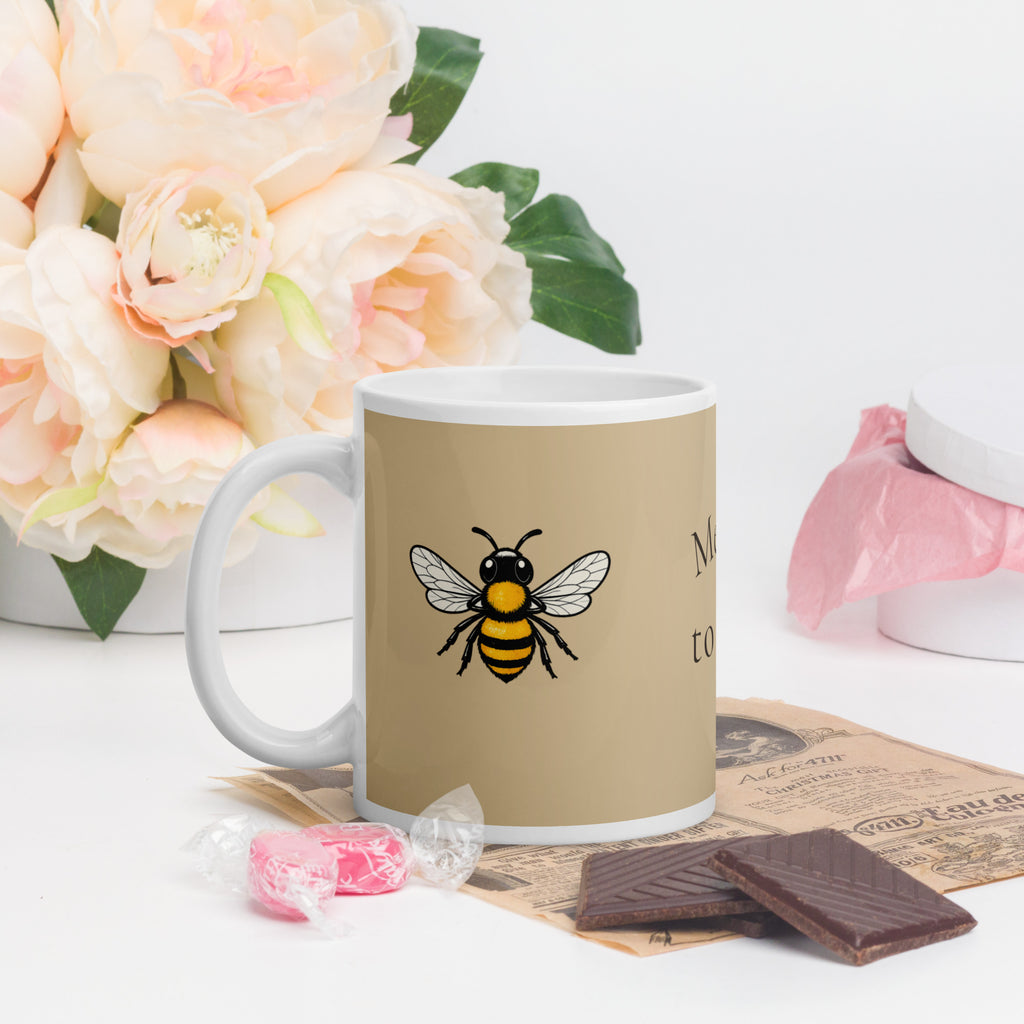 Beige ceramic coffee mug with white handle and rim, bee illustration on the front