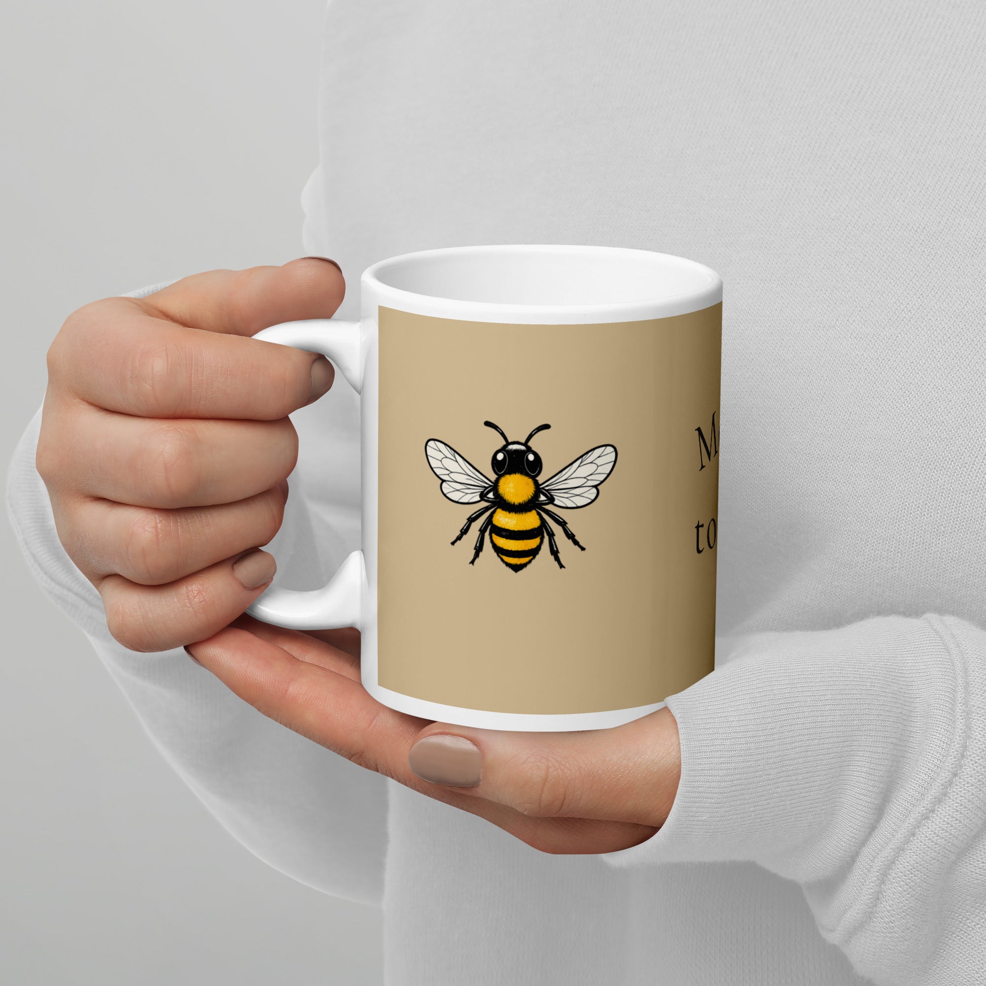Beige ceramic coffee mug with bee illustration, held close in hands