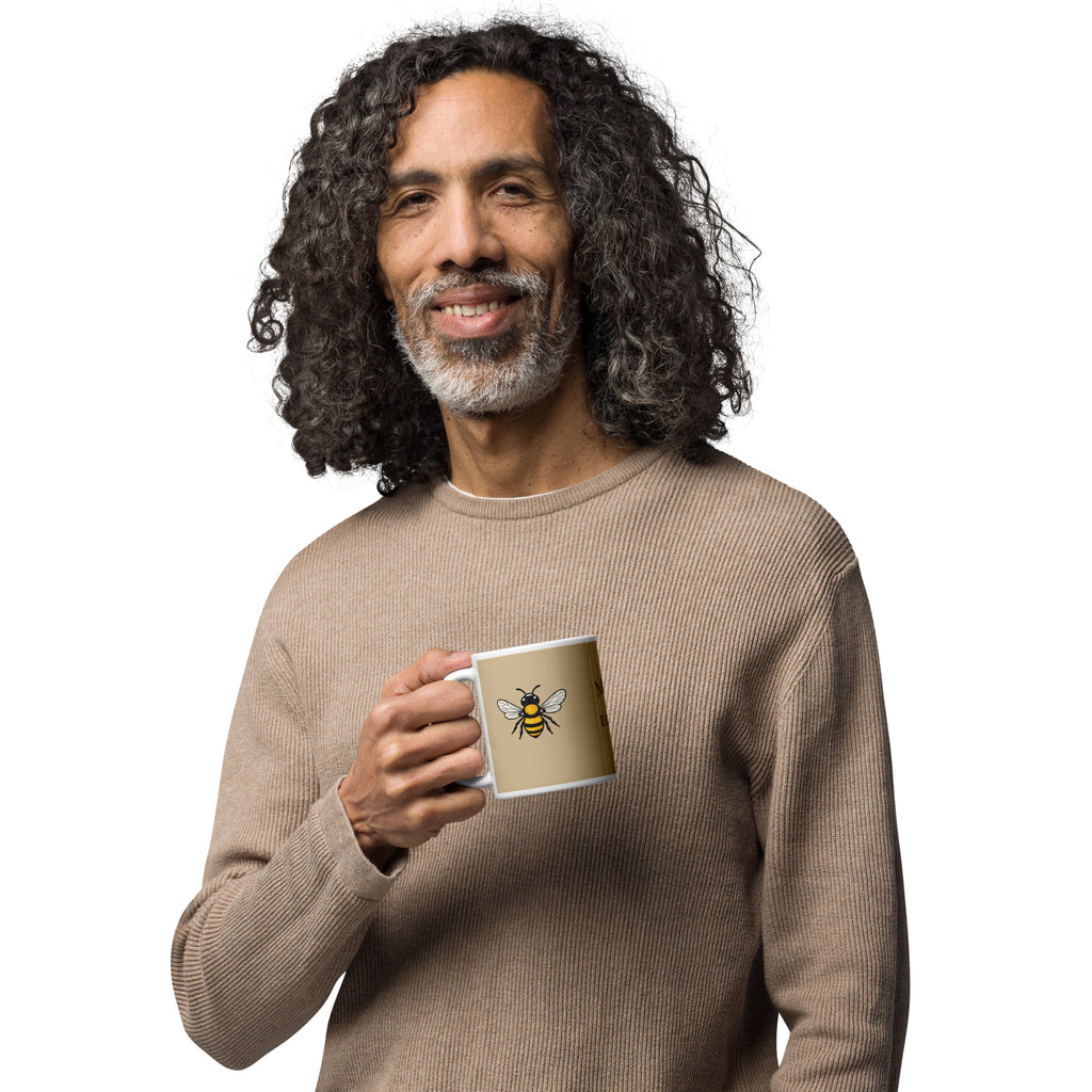 Person holding a beige ceramic mug with white handle and rim, yellow-and-black bee illustration