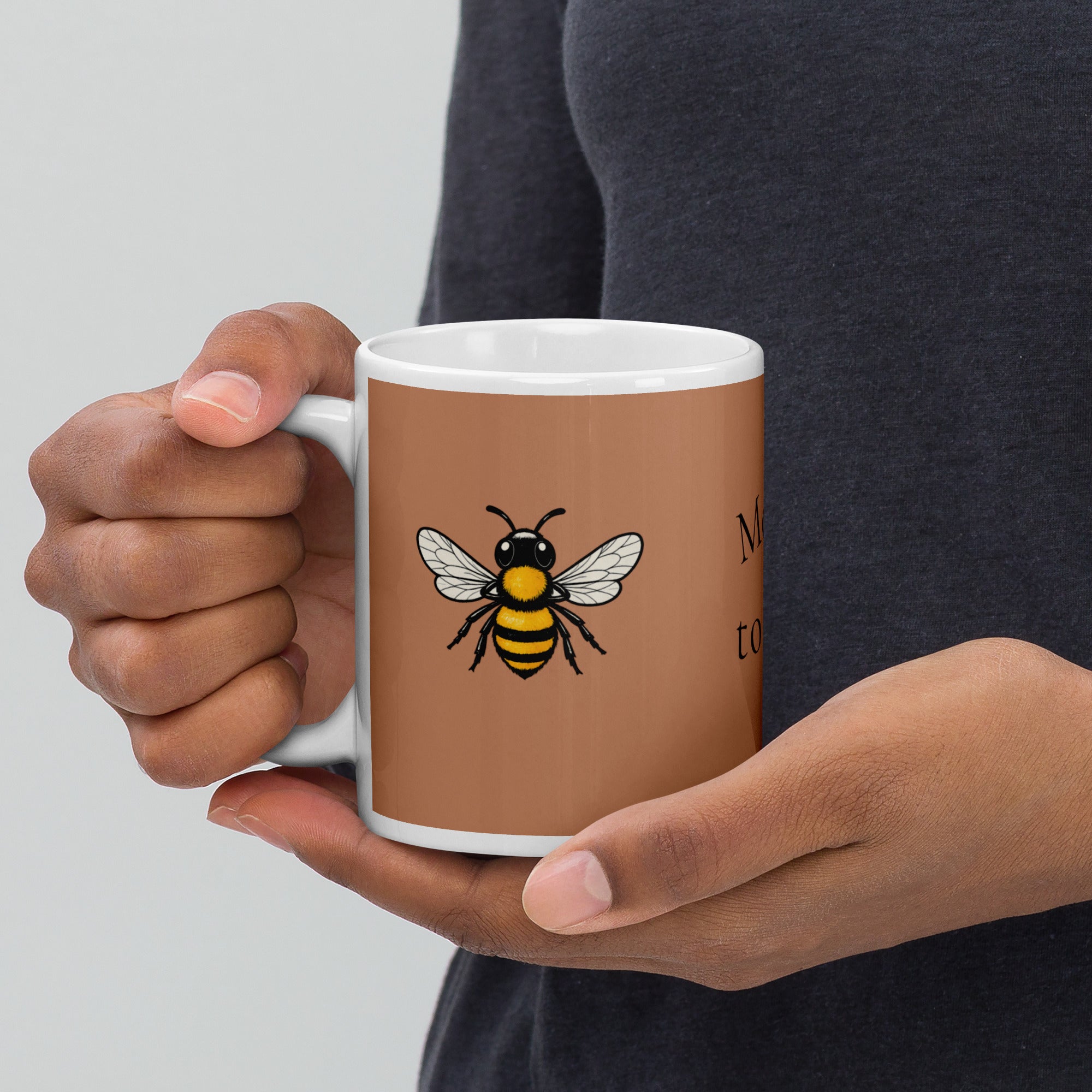 Brown ceramic mug with bee illustration, gripped by hands with white handle