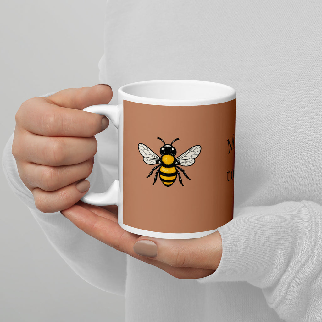 Brown ceramic mug with a bee graphic, held by hands in a white long-sleeve top.