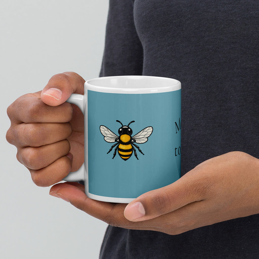 Blue ceramic mug with white rim and handle, bee illustration held in hands