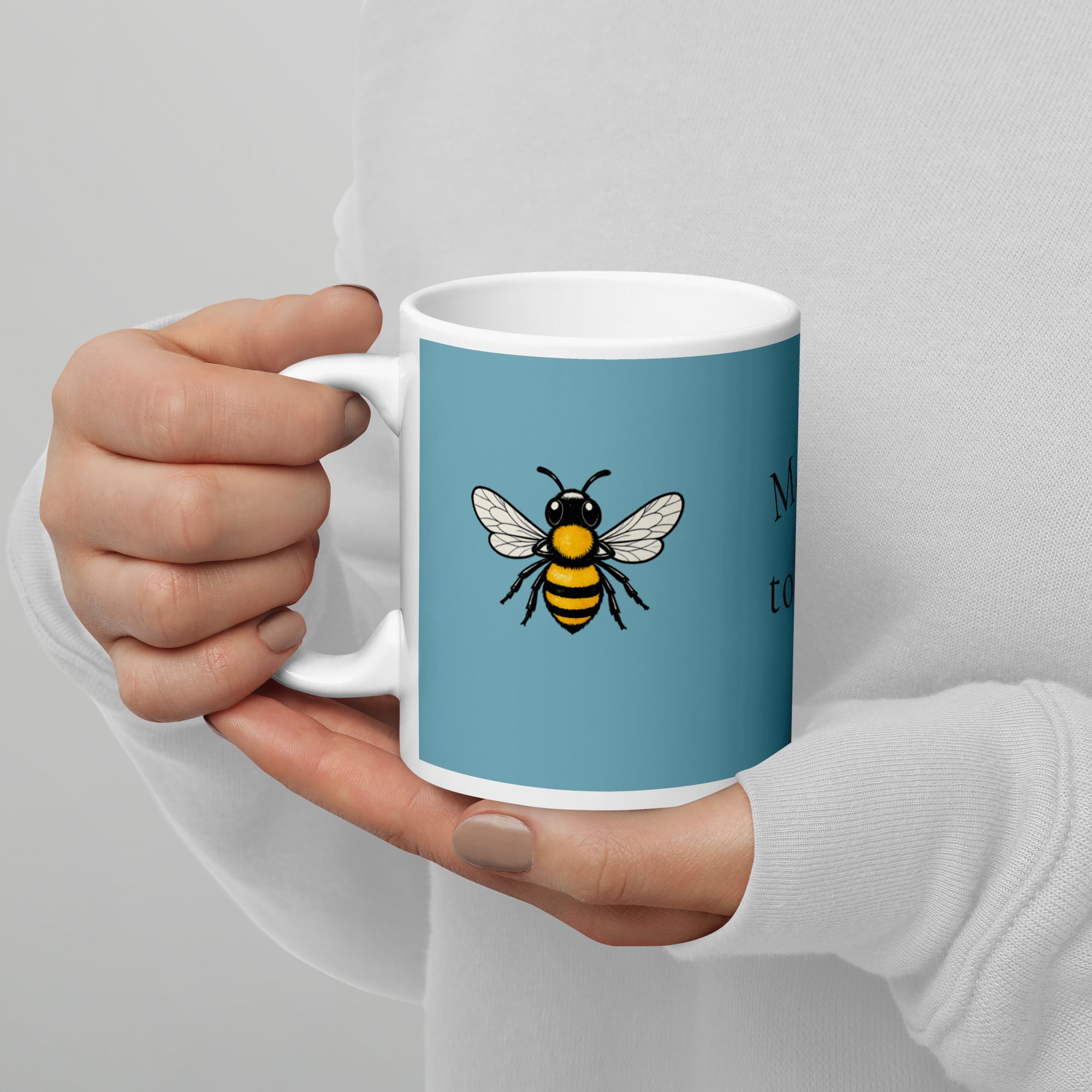 Blue ceramic mug with white rim and handle, bee illustration held by a person