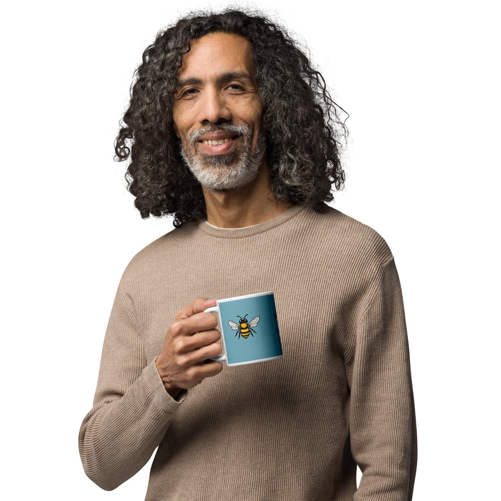 Blue ceramic coffee mug with bee illustration centered on front, white rim and handle