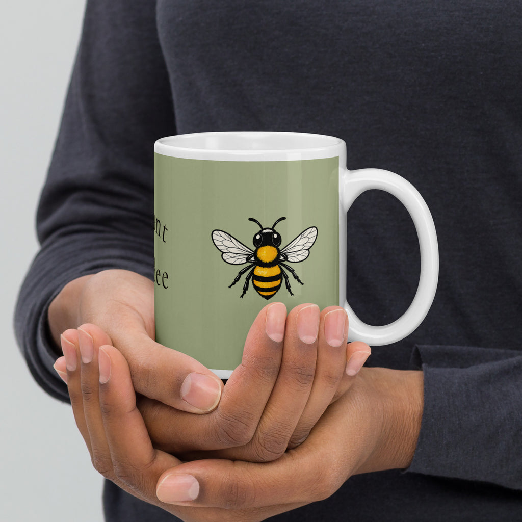 Sage green ceramic coffee mug with bee illustration, white handle, held by hands