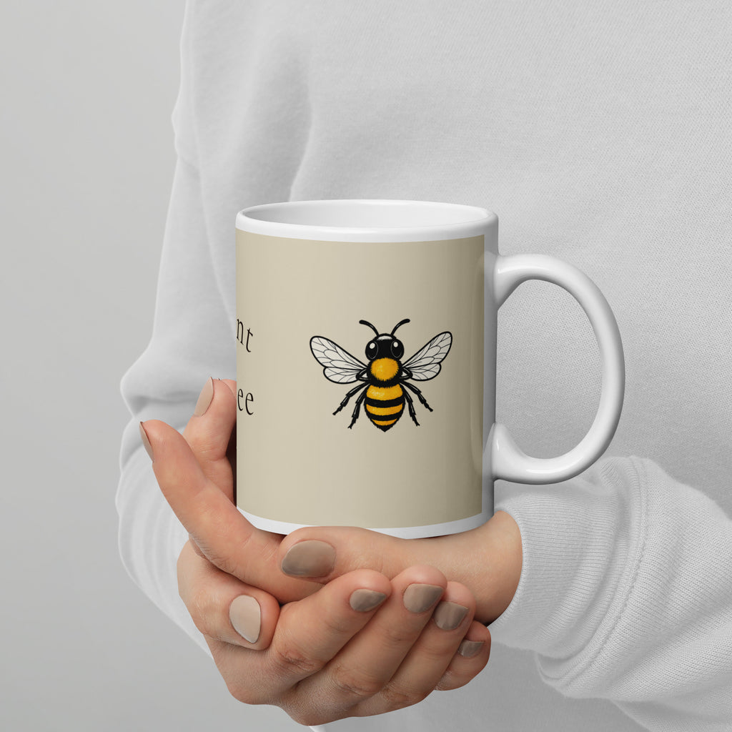 Light beige ceramic coffee mug with white handle, bee illustration and partial text
