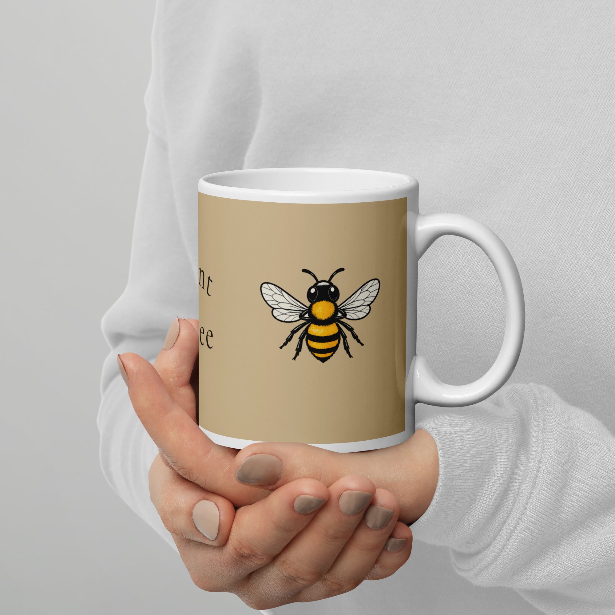 Beige ceramic coffee mug with white rim, holding hand, yellow-and-black bee illustration