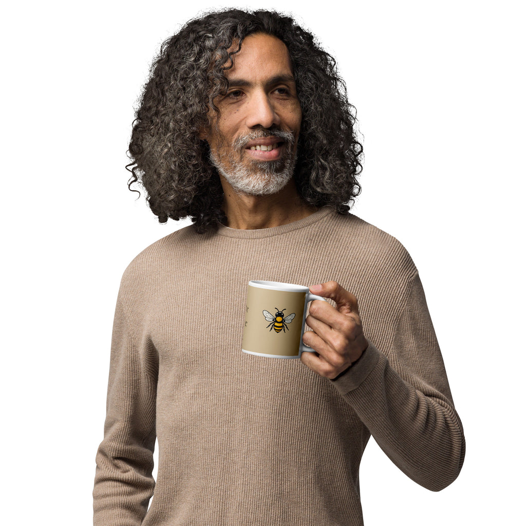 Person holding a beige ceramic mug with white rim and handle, yellow-and-black bee graphic