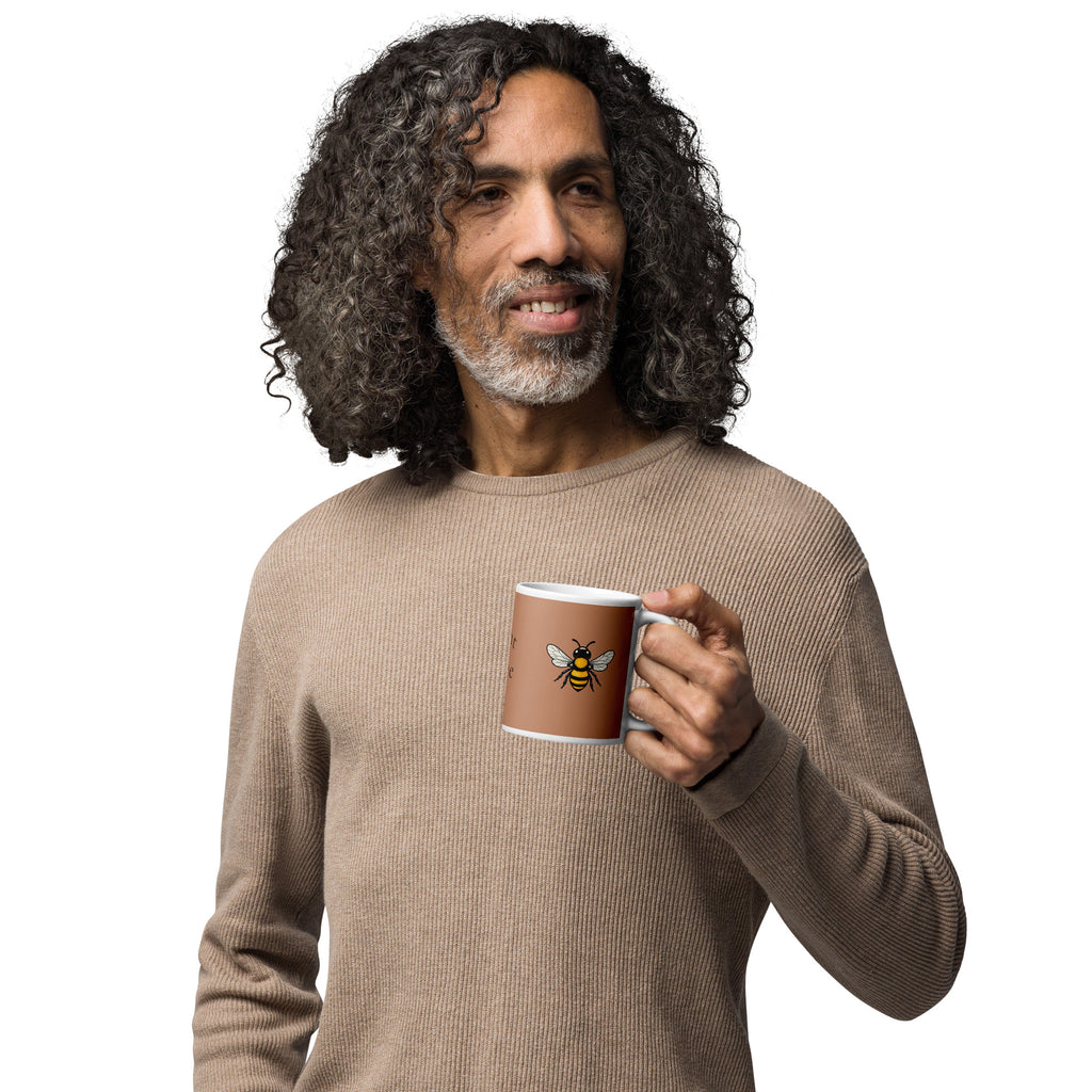 Brown ceramic mug with white rim and bee illustration, held in a hand