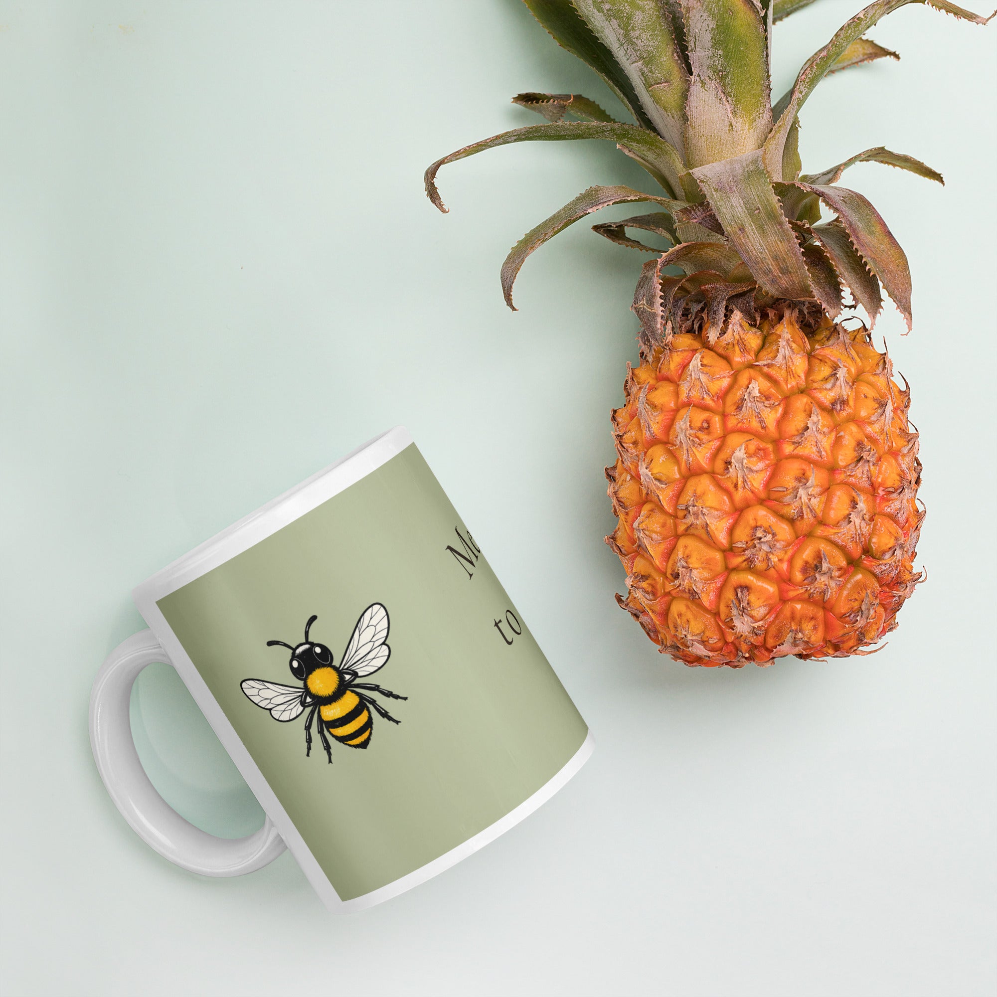 Sage green ceramic coffee mug with bee illustration, lying on a tabletop