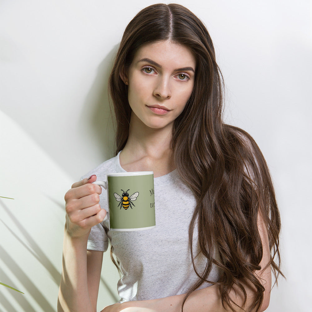 Sage green ceramic coffee mug with bee illustration, held in a woman’s hand