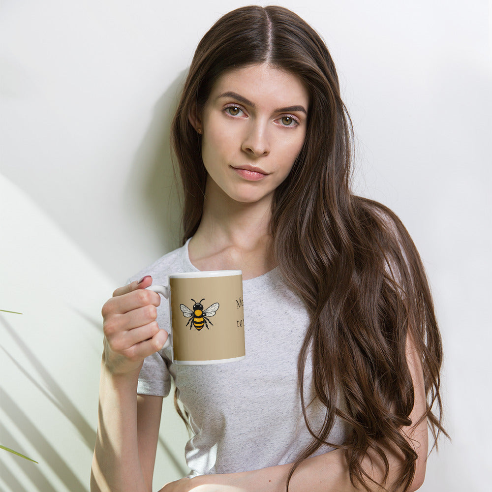 Beige ceramic coffee mug with bee illustration, held by a person in a light shirt