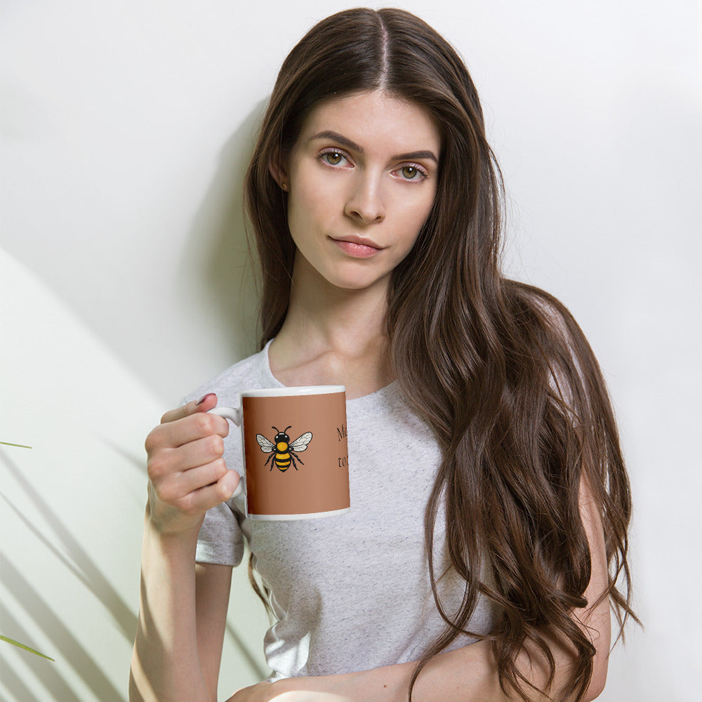 Brown ceramic mug with bee illustration, held near the face in one hand