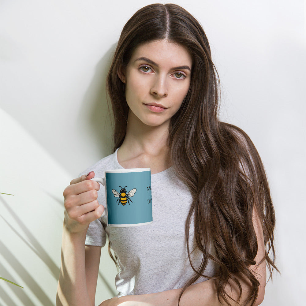 Person holding a blue ceramic coffee mug with a bee illustration