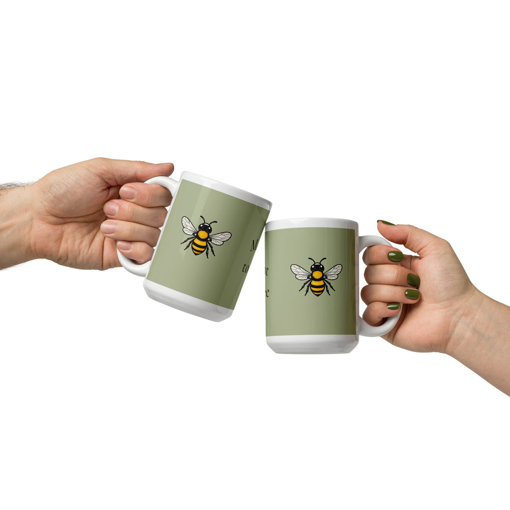 Sage green ceramic coffee mug with bee illustration, held with another matching mug