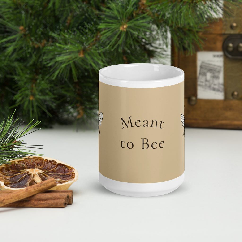 Beige ceramic coffee mug with white top and base, text reading "Meant to Bee"