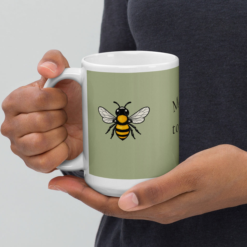 Sage green ceramic coffee mug with bee illustration, white handle, held by hands