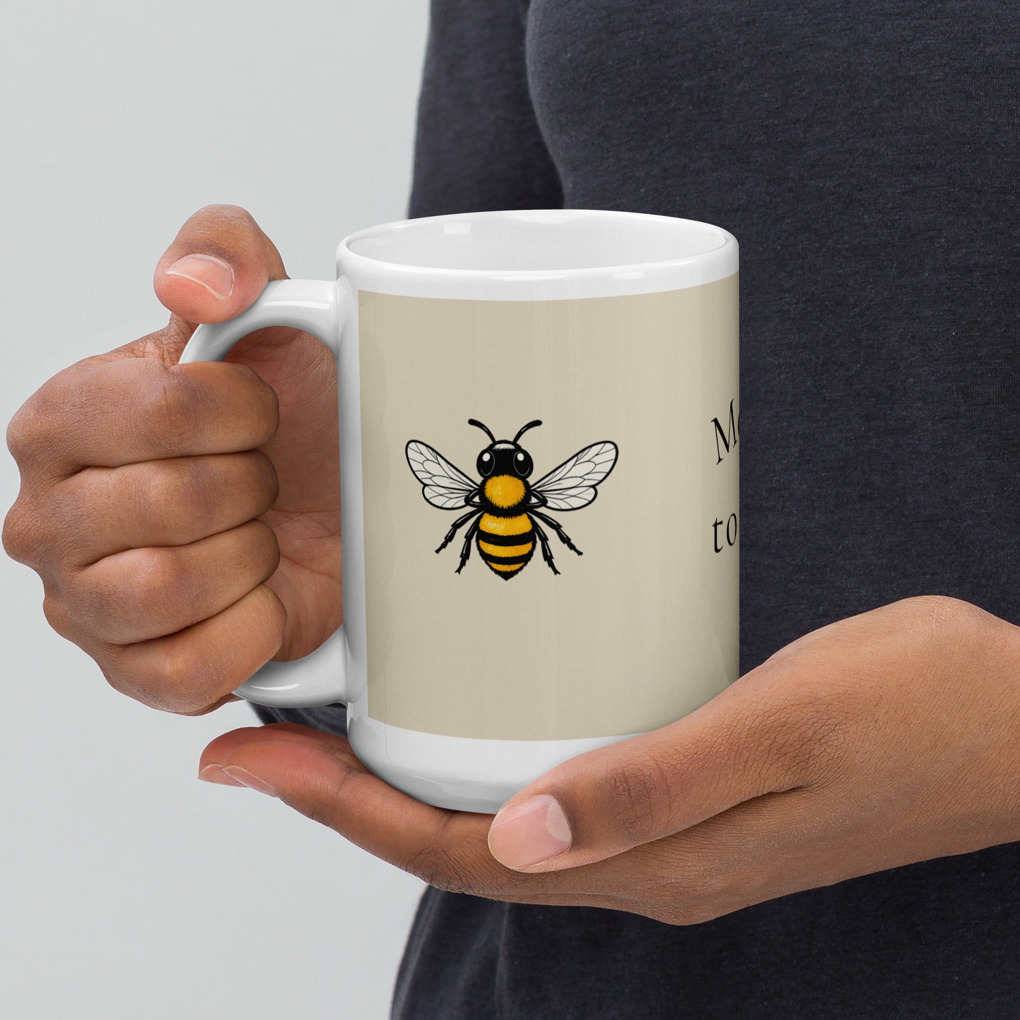 Light beige ceramic coffee mug with white handle, bee illustration and partial text