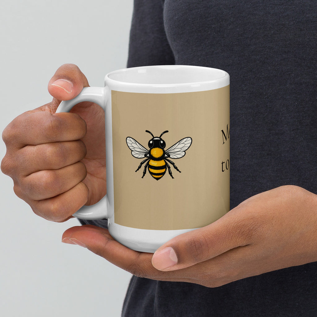 Beige ceramic coffee mug with white handle and rim, centered bee illustration on front