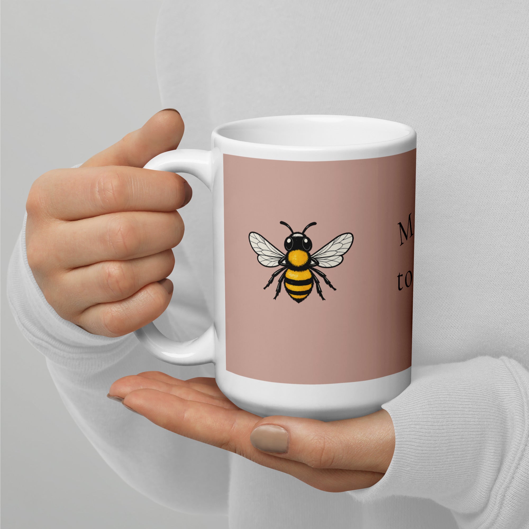 Dusty rose ceramic mug with bee illustration and white handle, held in hands