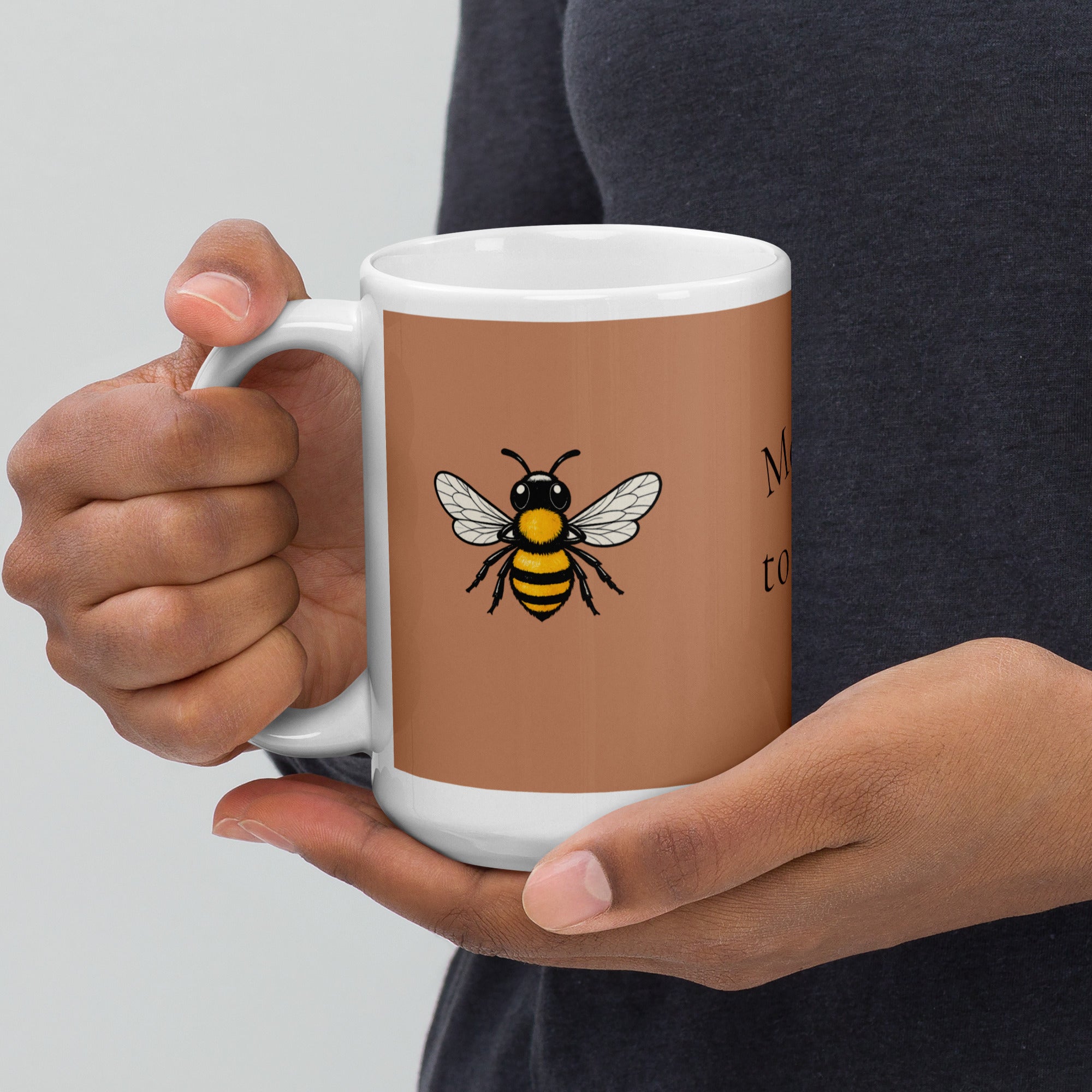 Brown ceramic mug with bee illustration, close-up of hands gripping the white handle.