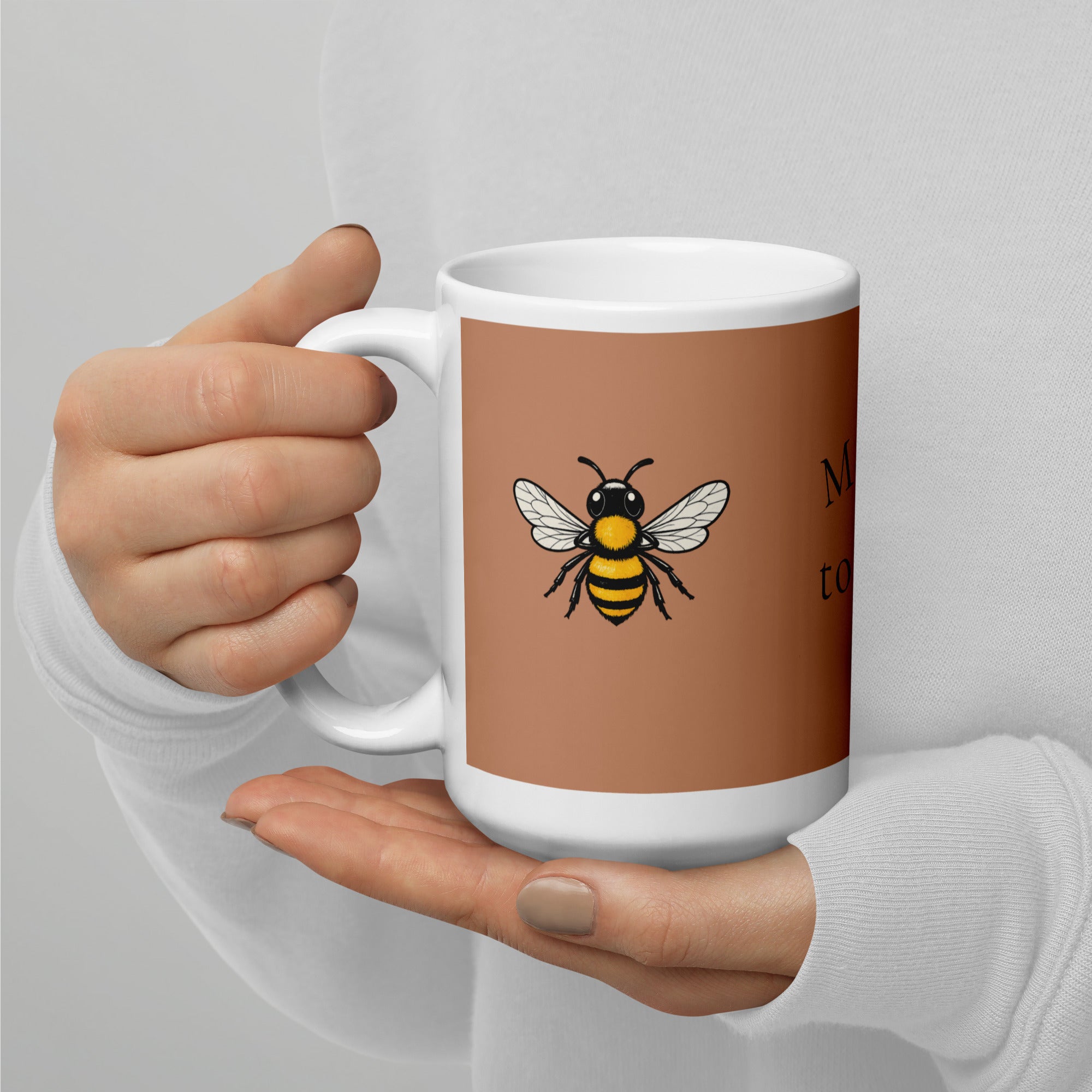 Brown ceramic mug with bee illustration, angled view with one hand on the handle.
