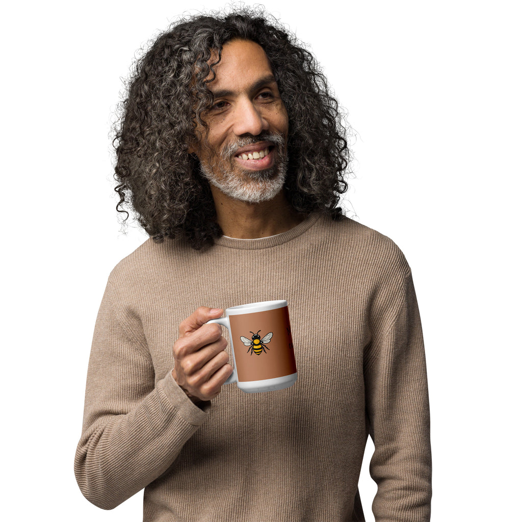 Brown ceramic mug with white rim and handle, yellow bee illustration; person holding mug