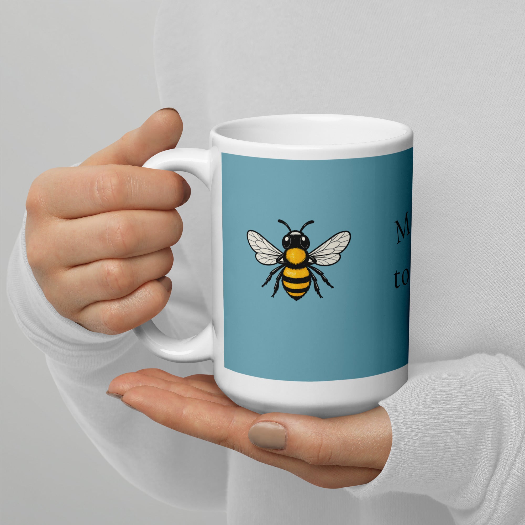Blue ceramic coffee mug with bee illustration held close in hands