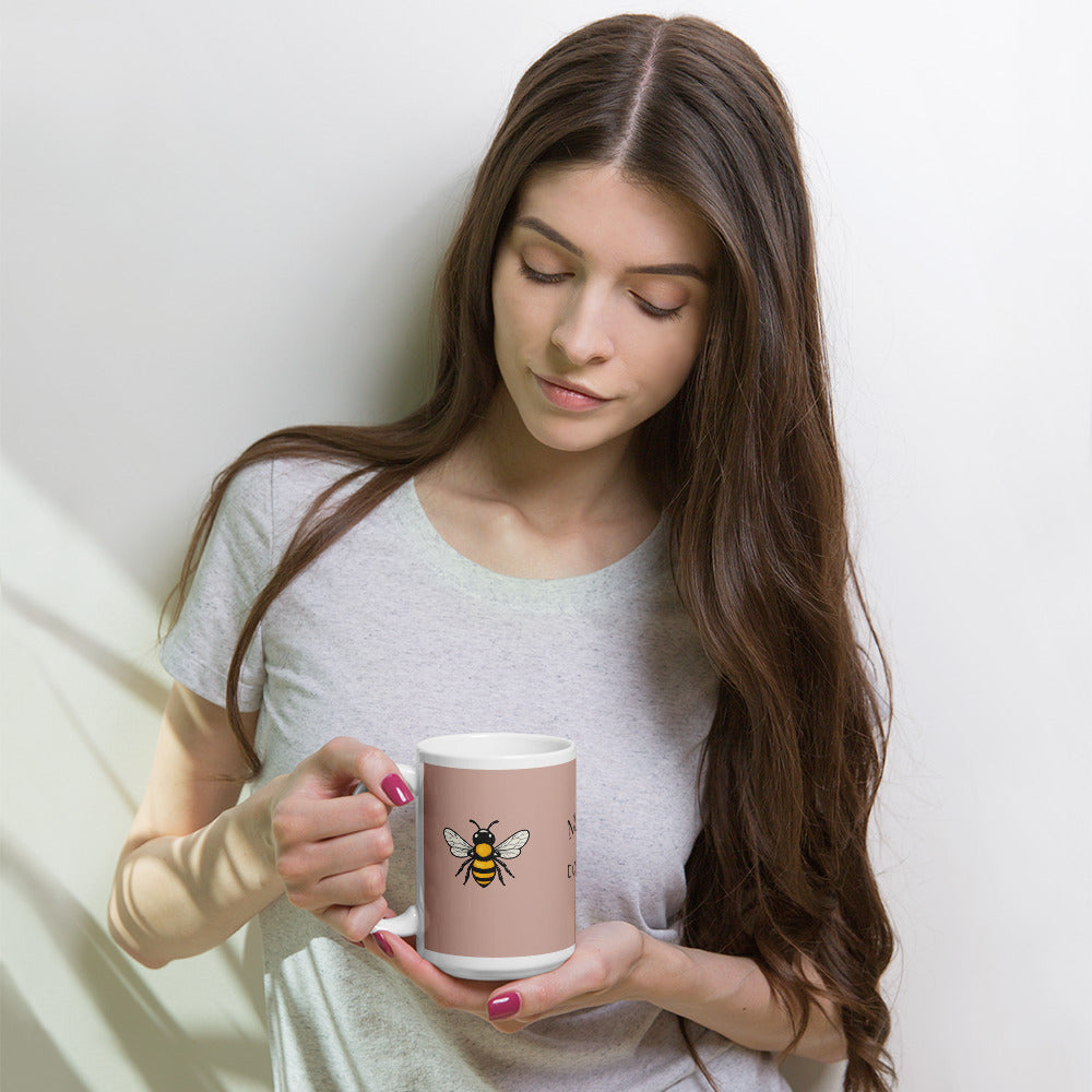 Dusty rose ceramic mug with white rim and handle, held in hands with bee illustration.