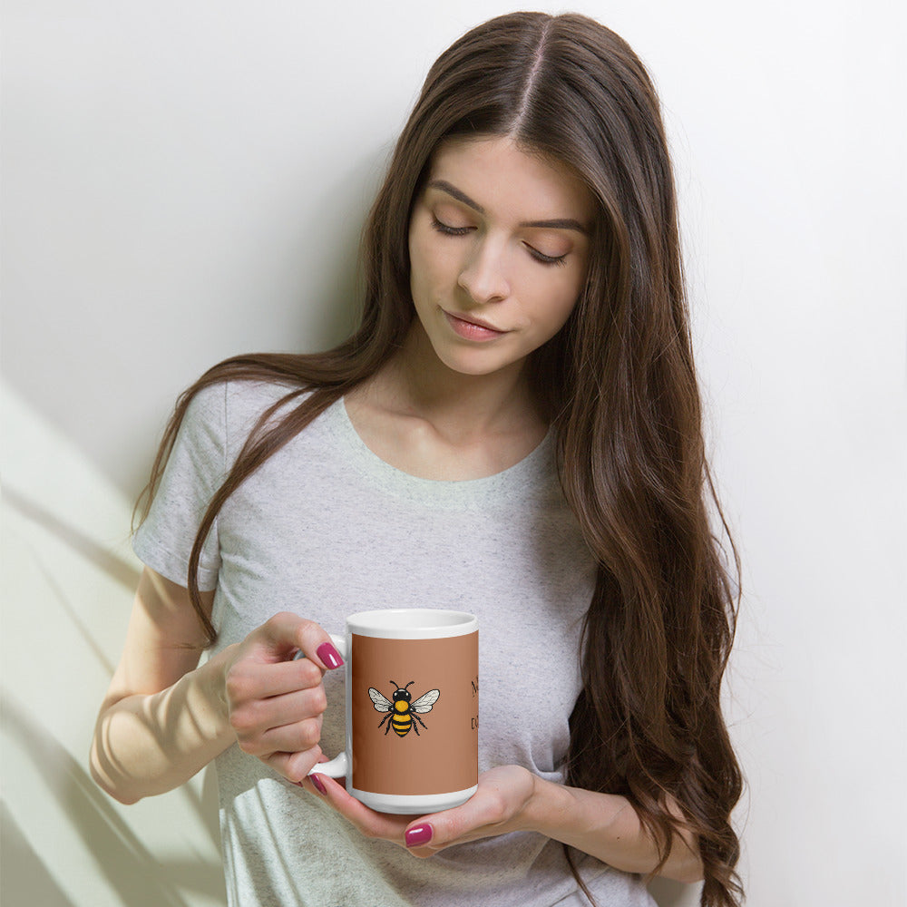 Ceramic coffee mug in brown with bee illustration, held in both hands with nails painted red.