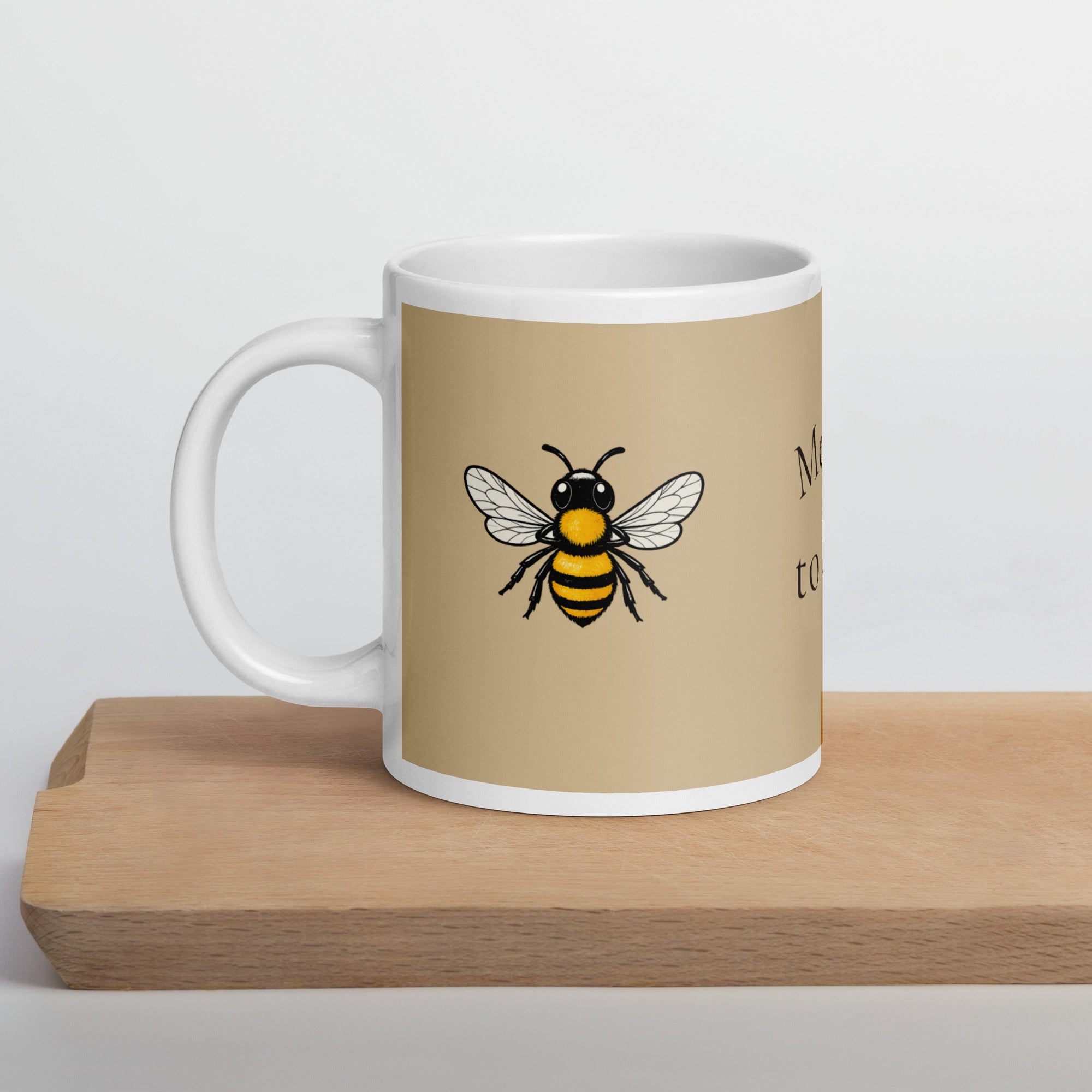 Beige ceramic coffee mug on a wooden surface, with a centered bee illustration
