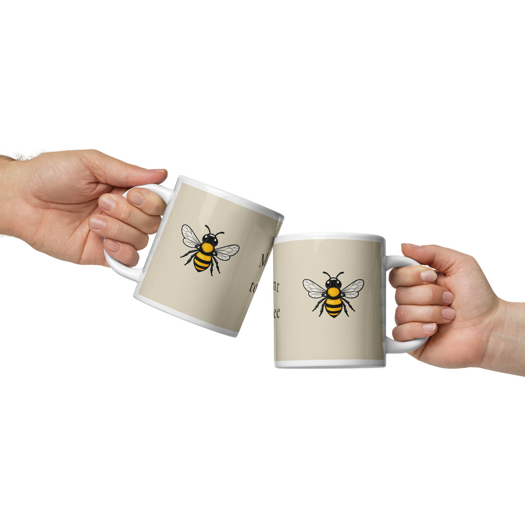 Light beige ceramic coffee mug, bee illustration, shown with another mug held nearby