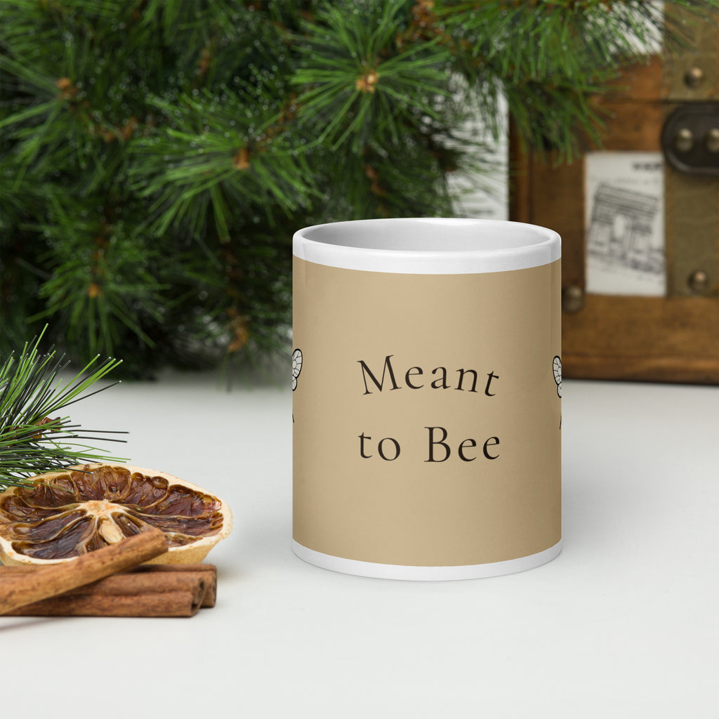 Beige ceramic coffee mug with white rim and base, "Meant to Bee" text on front