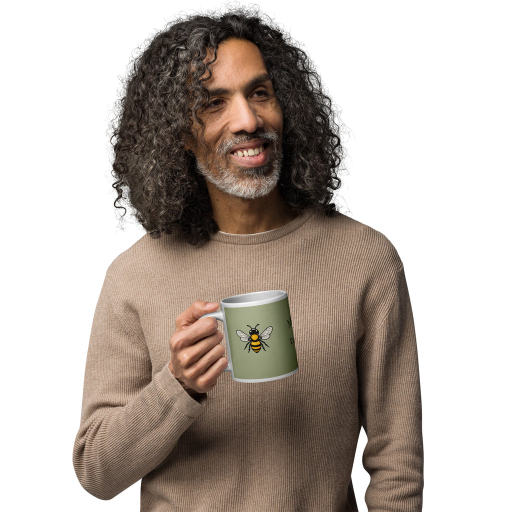 Sage green ceramic coffee mug with bee illustration, held at mid-chest