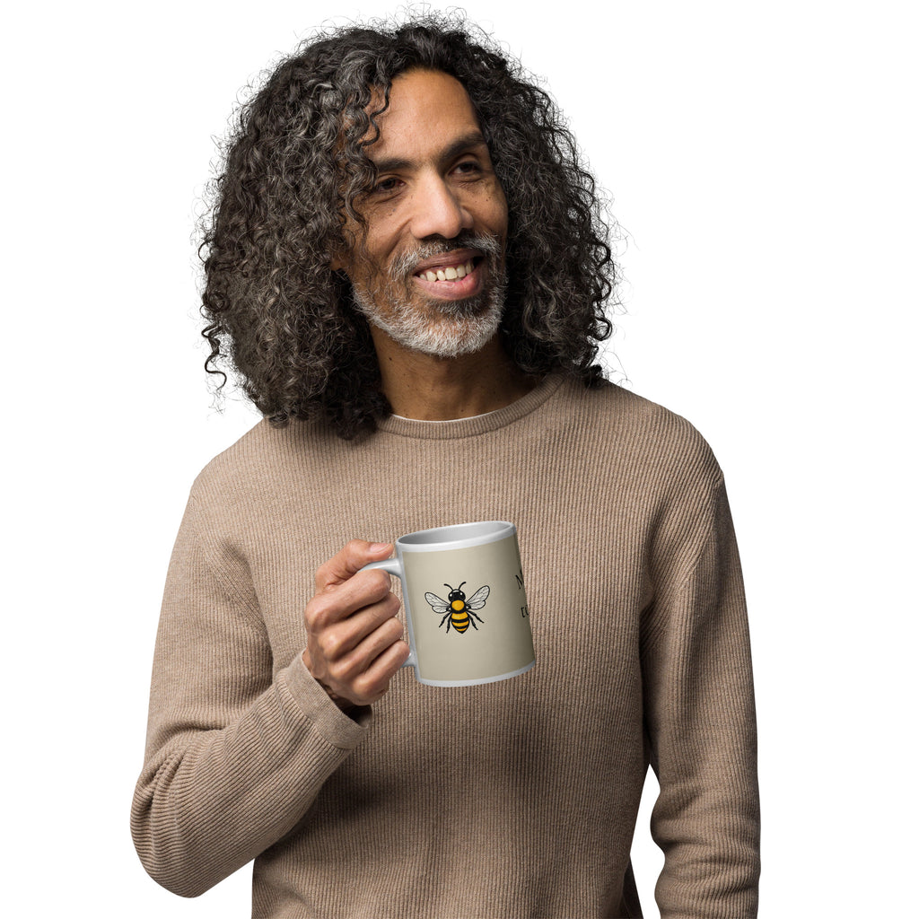 Light beige ceramic coffee mug with bee illustration, held near chest