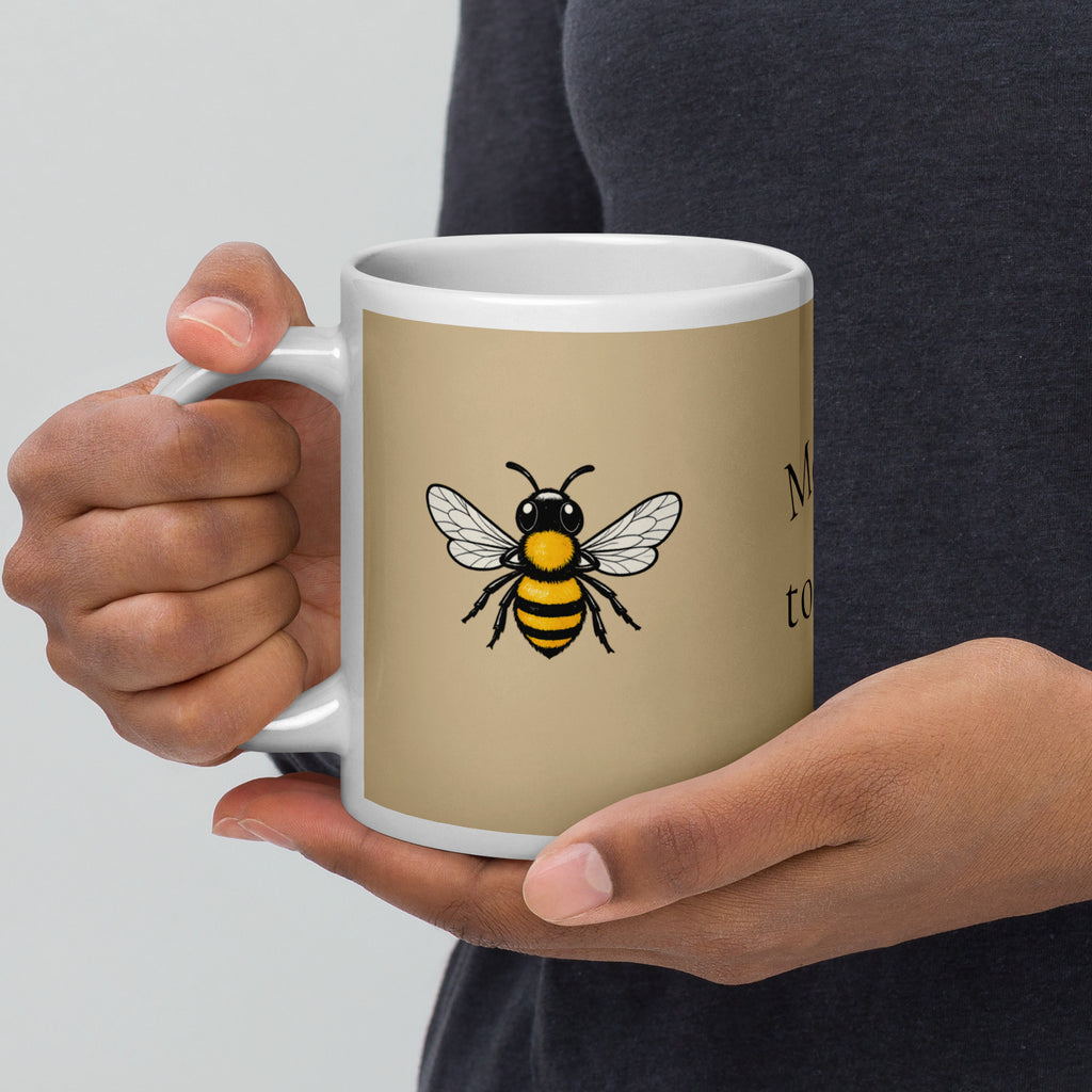 Beige ceramic coffee mug with white rim and handle, bee illustration and partial text