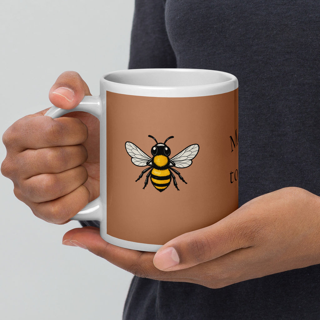 Brown ceramic coffee mug with bee illustration centered on the front, hands holding the sides.