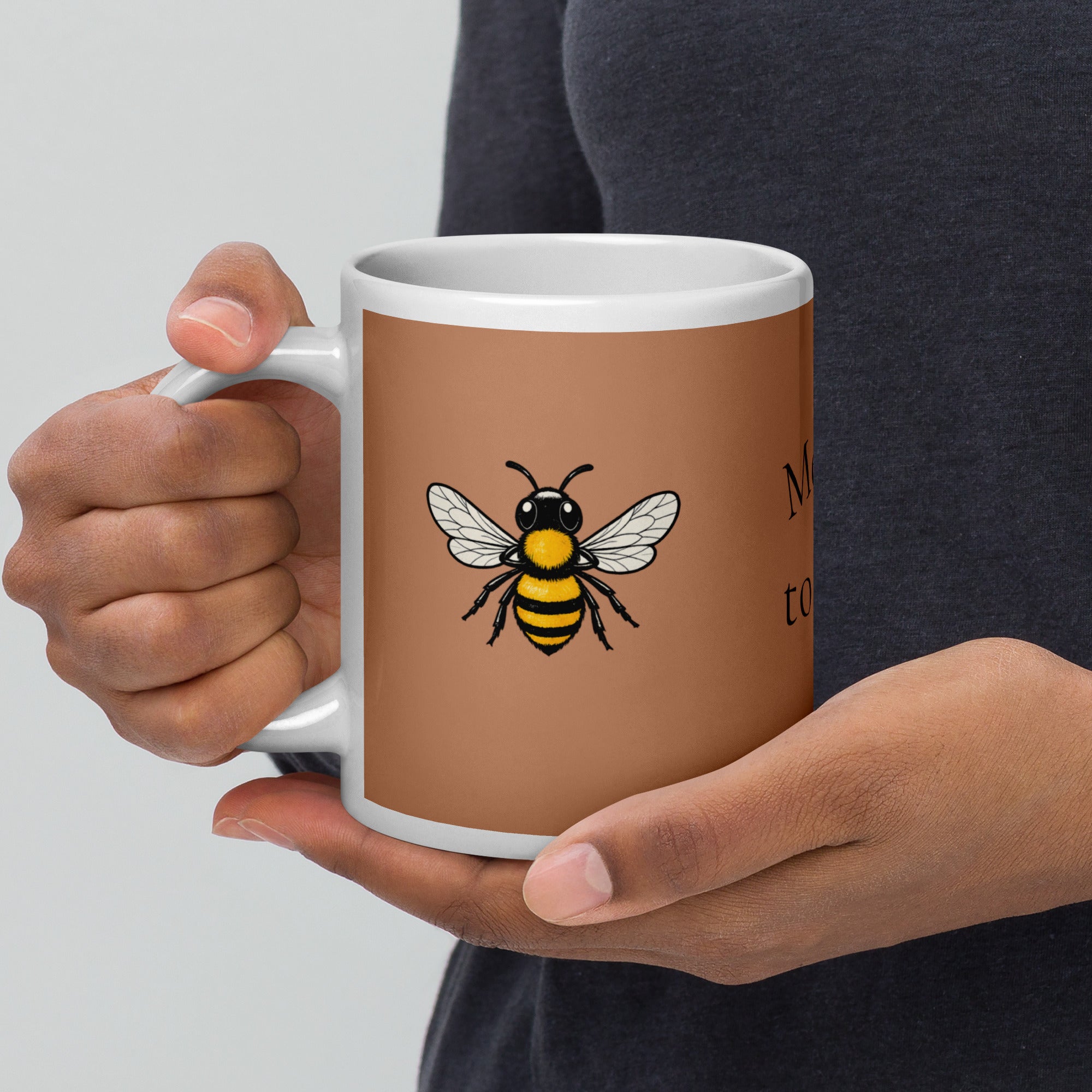 Brown ceramic coffee mug with bee illustration centered on the front, hands holding the sides.