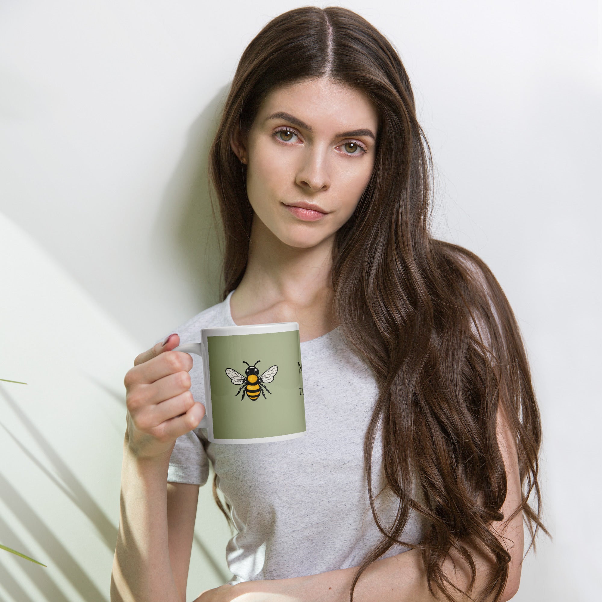 Sage green ceramic coffee mug with bee illustration, held near the chest