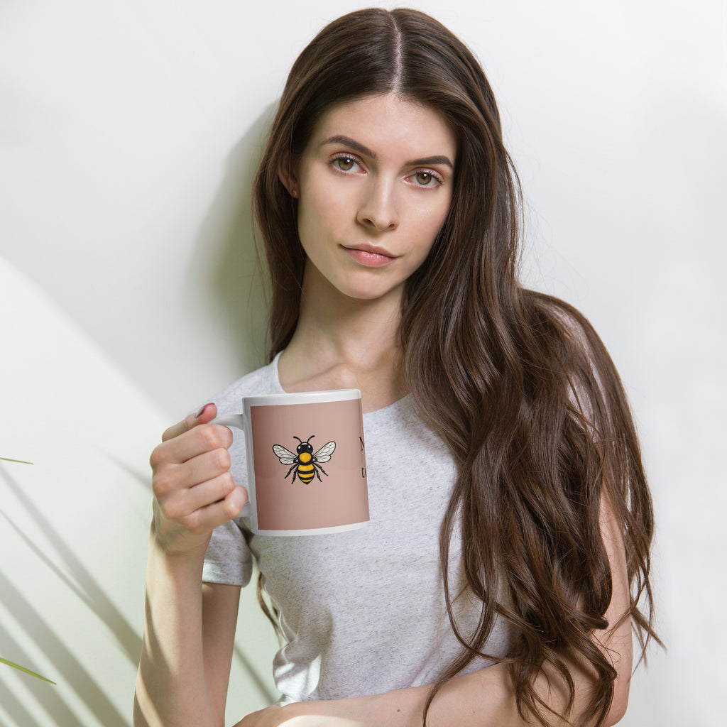 Person holding a dusty rose ceramic mug with bee illustration and white rim